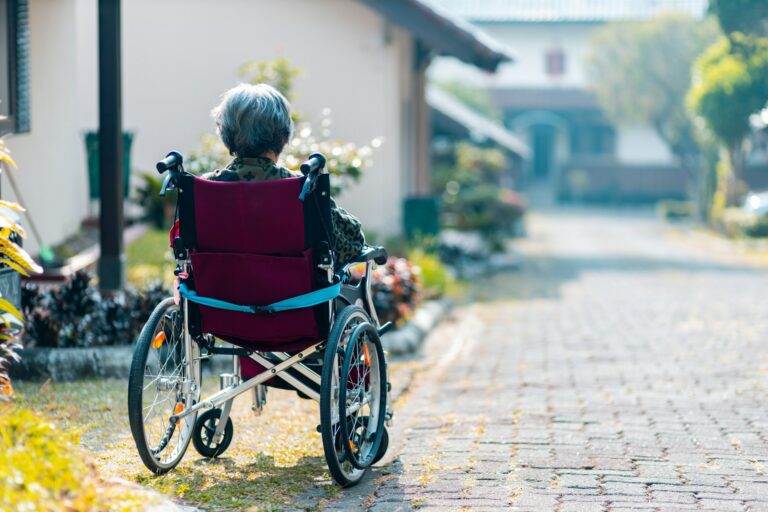 Older woman sitting in a wheelchair outside of a house